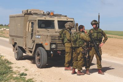 IDF soldiers stand beside an armored military vehicle